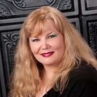 A woman with long blonde hair is wearing a black shirt and smiling for the camera.