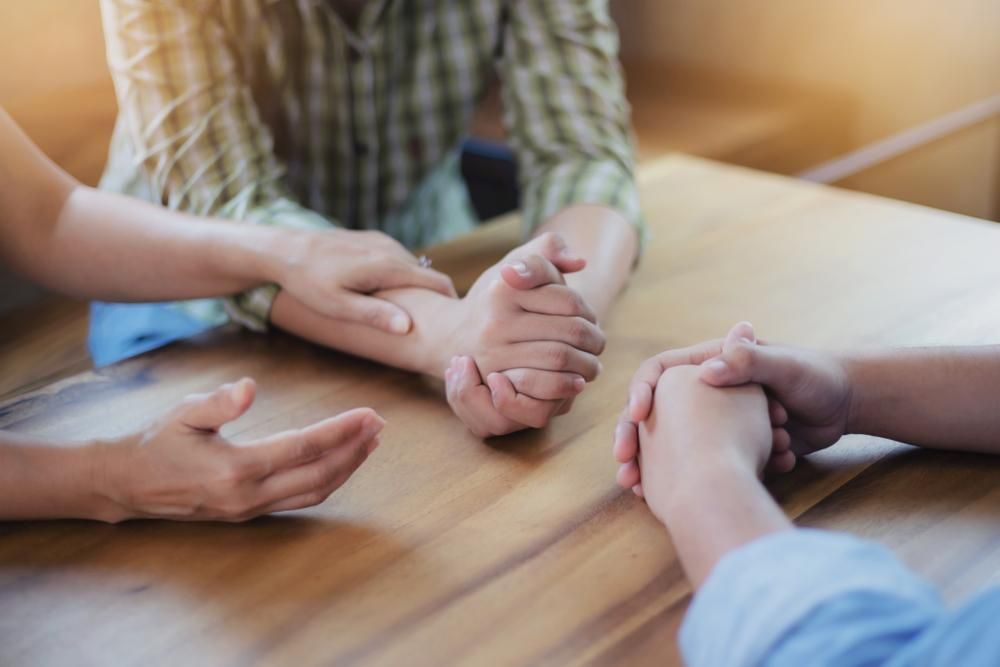 A Group Of People Are Sitting At A Table Holding Hands — Active Ables Community Services In Tamworth, NSW