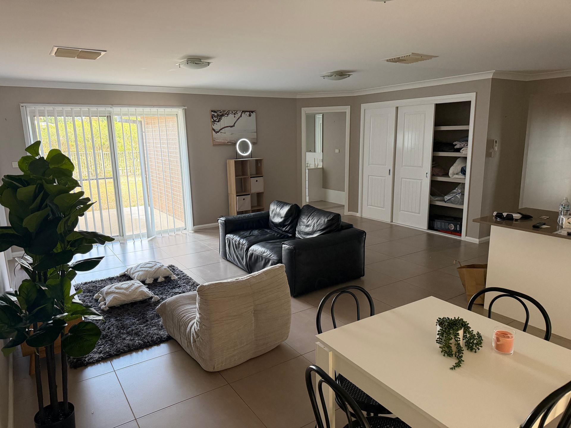 Bright modern living room with black leather sofa, white chairs, dining table, and sliding glass doors. — Active Ables Community Services In Tamworth, NSW