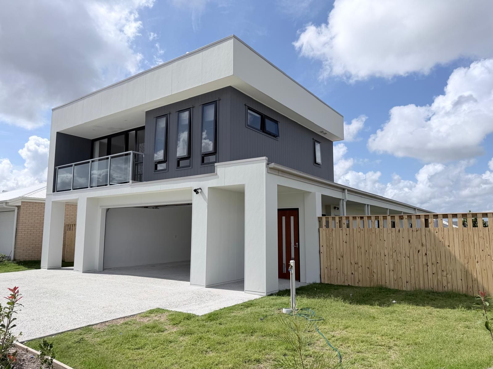 Modern two-story house with white and gray exterior, balcony, garage, and grassy yard under a blue sky