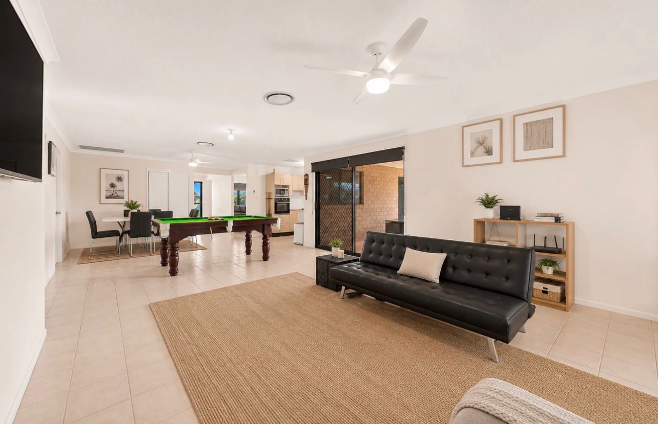 Modern open-plan living room with black sofa, beige rug, and pool table in the background