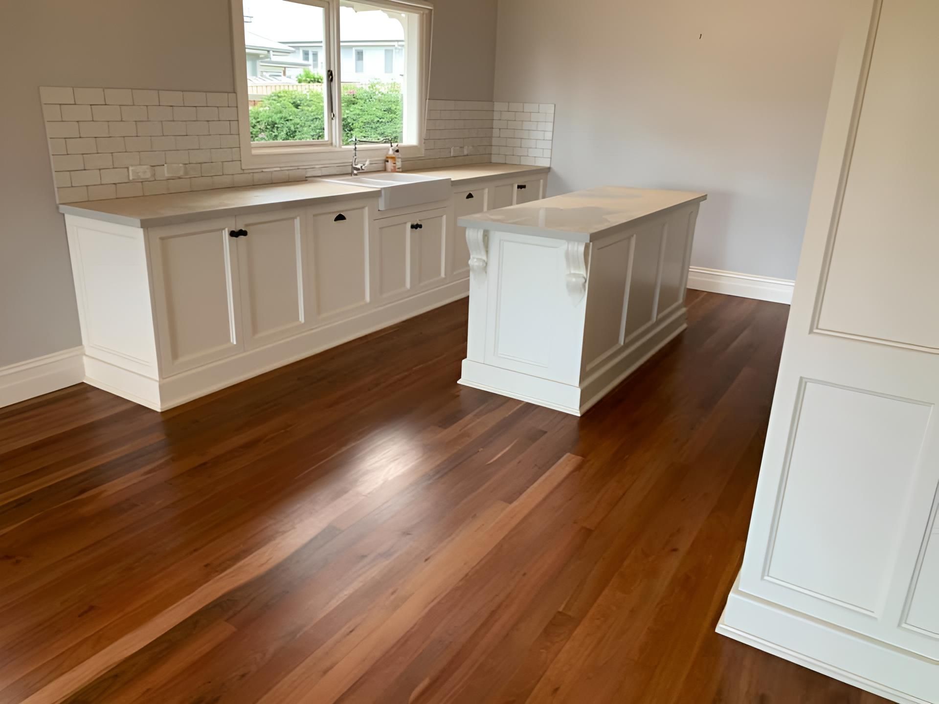 An empty kitchen with hardwood floors and white cabinets — Coolangatta Floor Sanding In Shoalhaven Heads, NSW