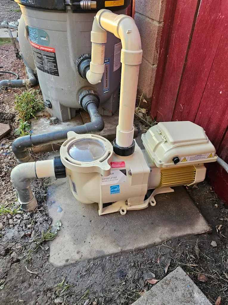 Pool pump system, beige pump and filter, connected with PVC pipes, outdoor setting.