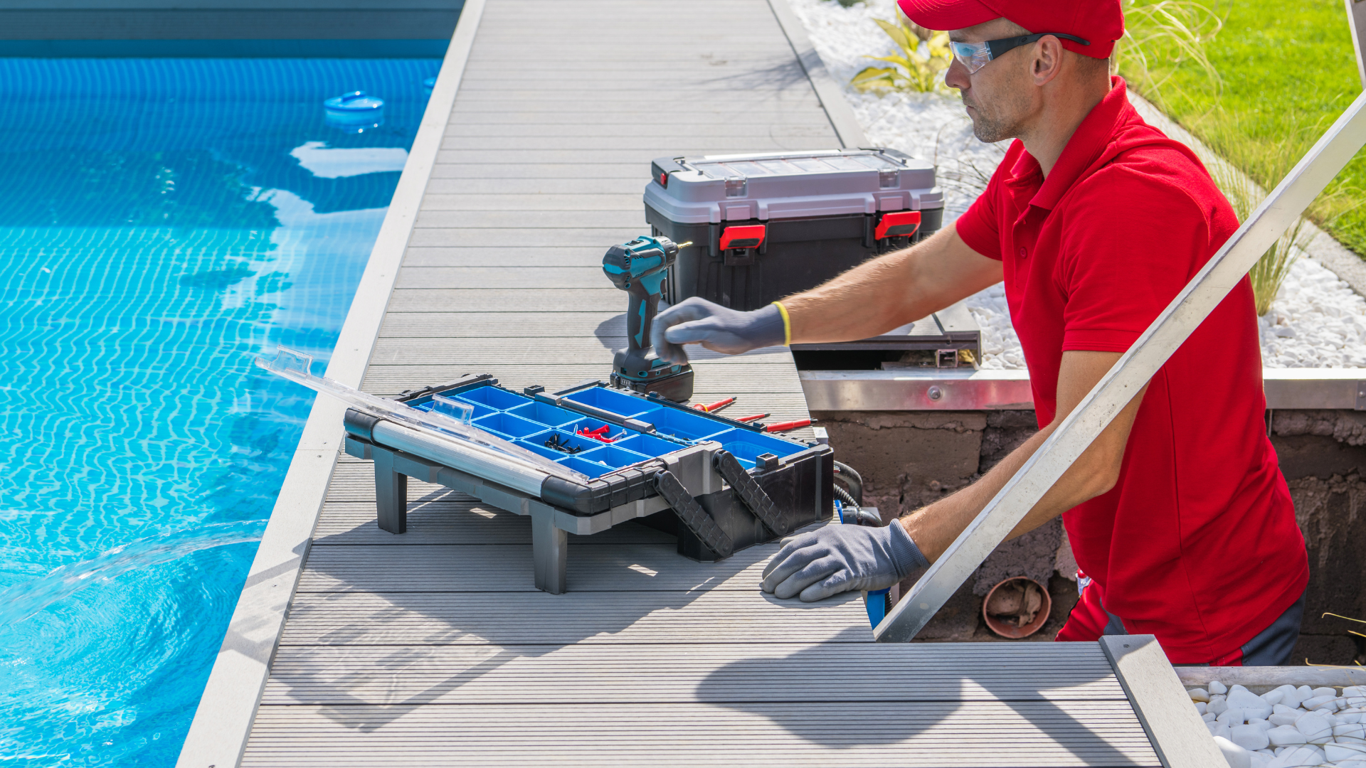 Pool technician in a red uniform performing maintenance work by the pool, using tools and a toolbox to ensure proper functioning of the pool system.