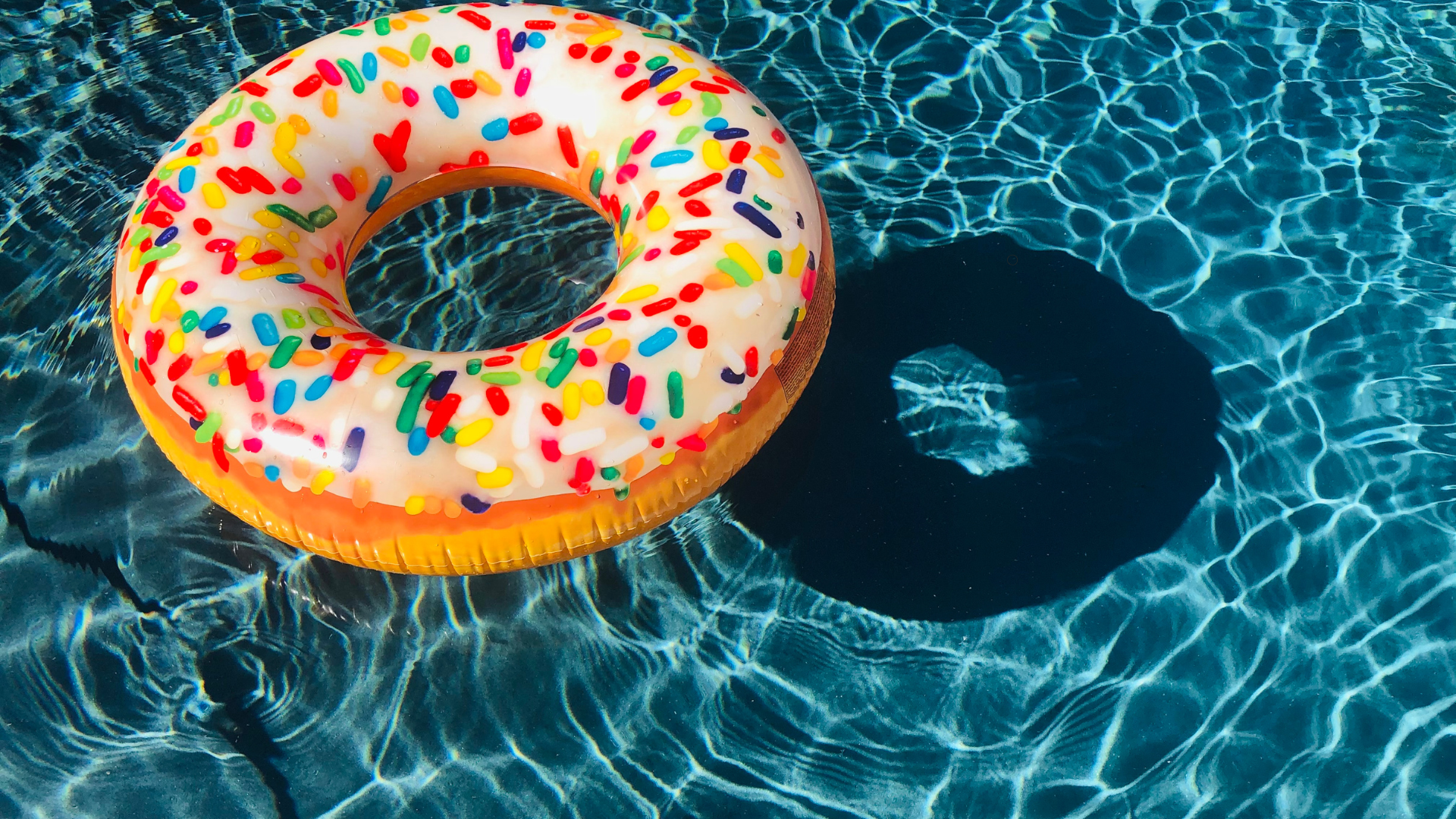 Colorful donut-shaped pool float floating in crystal-clear pool water, showcasing a fun and inviting atmosphere in a well-maintained pool.