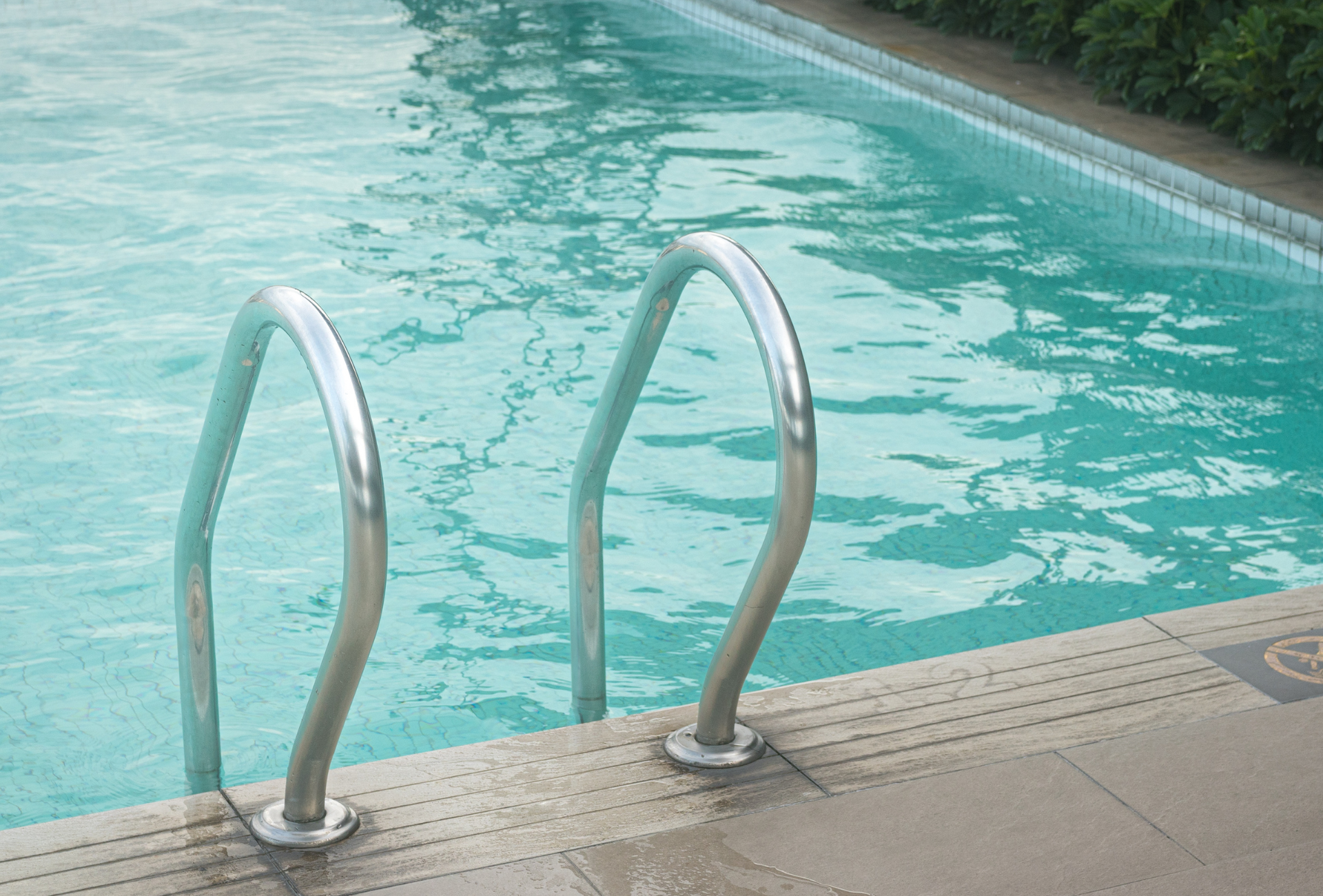 Pool with metal handrails. Turquoise water and a stone deck.