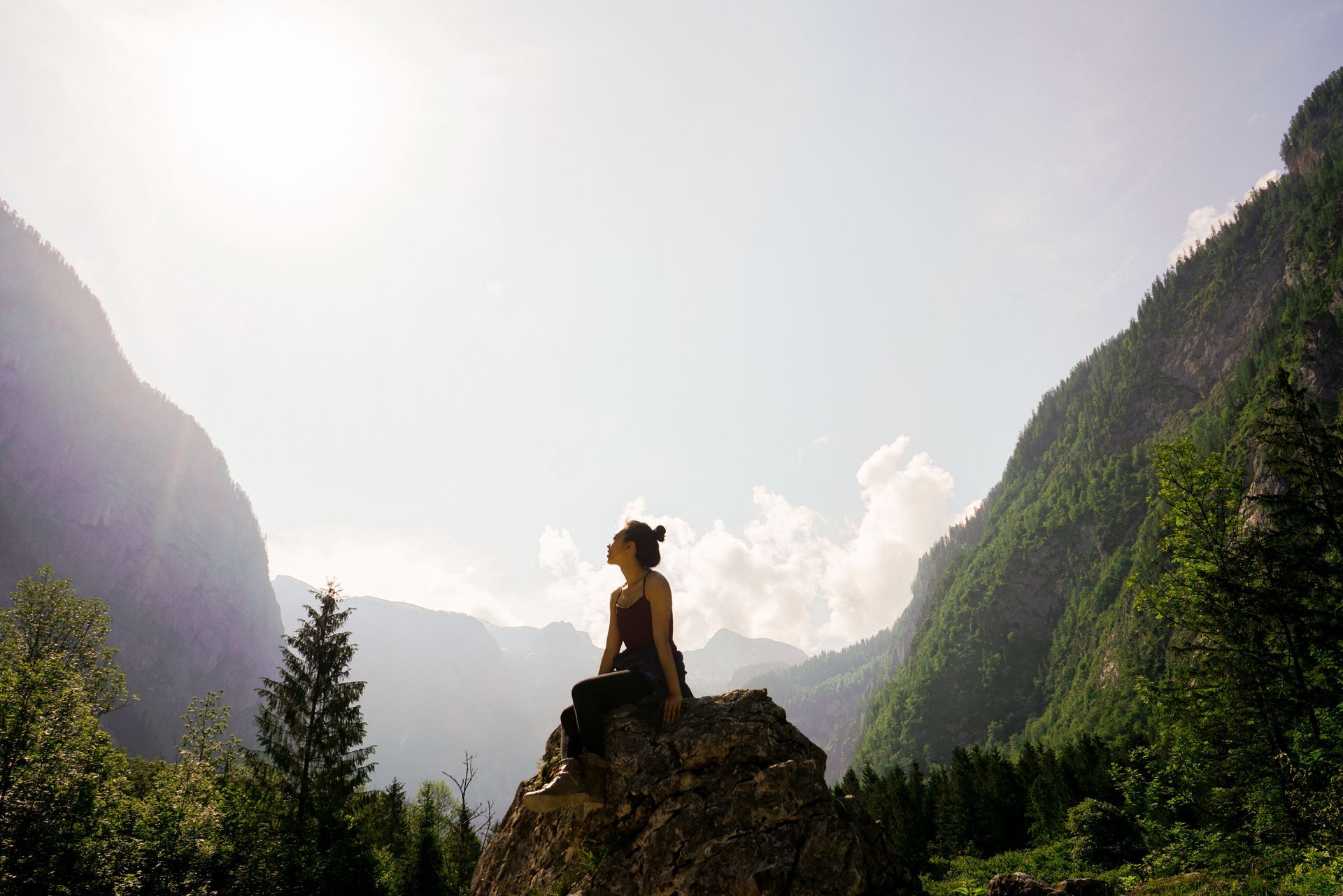 Silhouette of a person on a rock overlooking a sunlit mountain valley