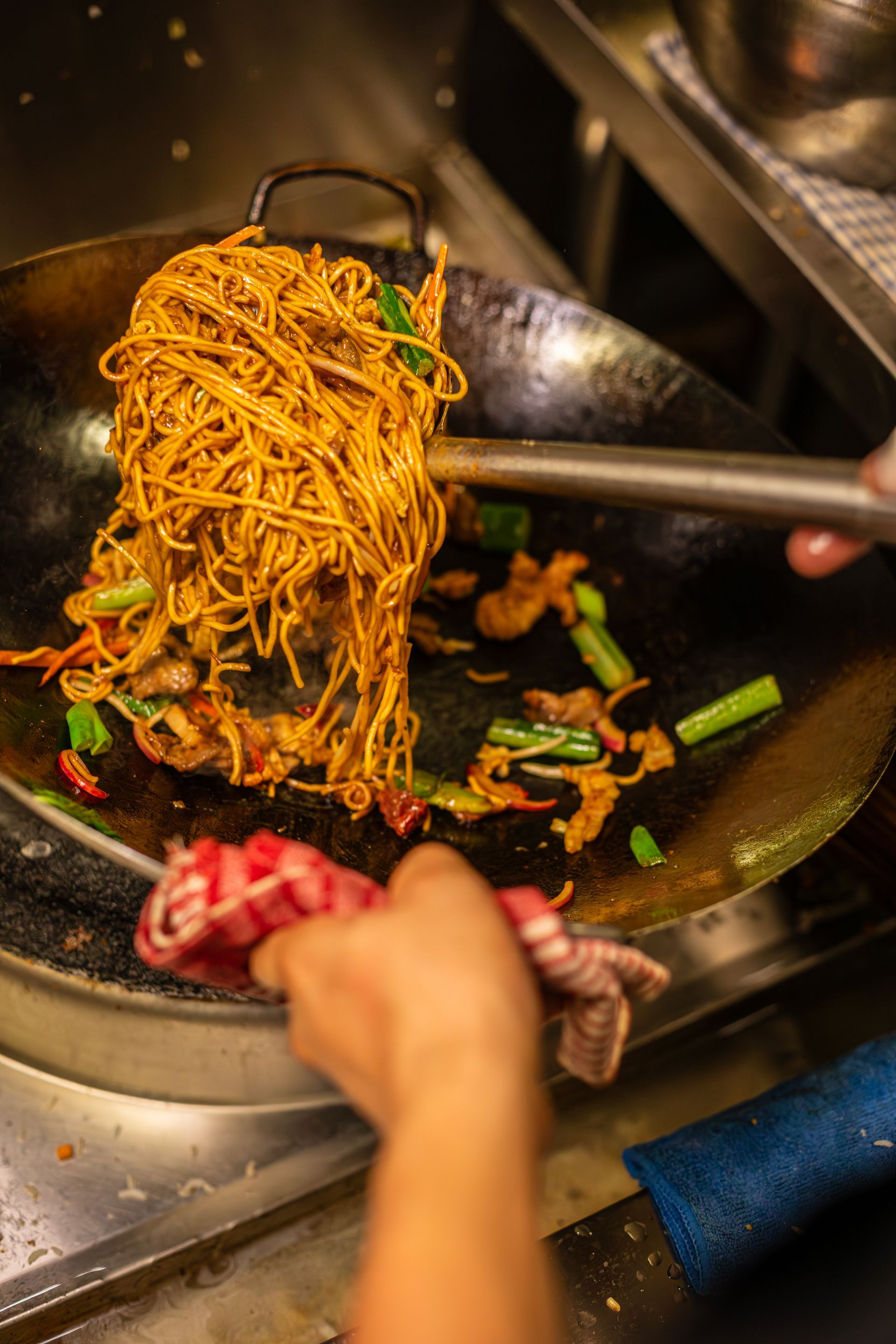 A person is cooking noodles and vegetables in a wok.