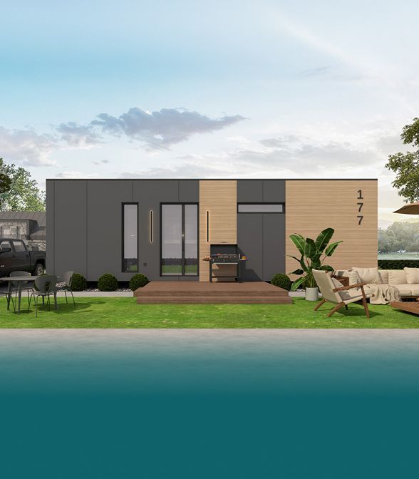 Modern cabin exterior: gray and wood siding, deck, grill, lawn, outdoor seating, and water view.