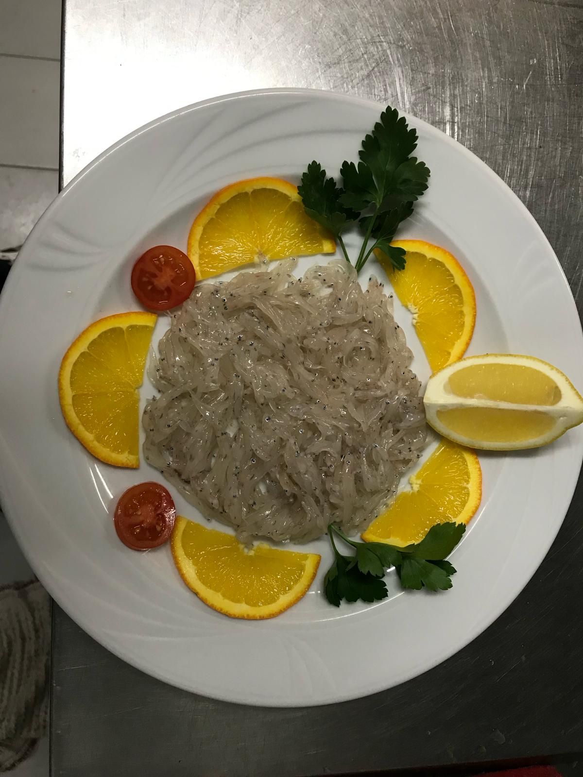 Piatto di cibo preparato, probabilmente frutti di mare, decorato con fette d'arancia, pomodori, prezzemolo e limone.