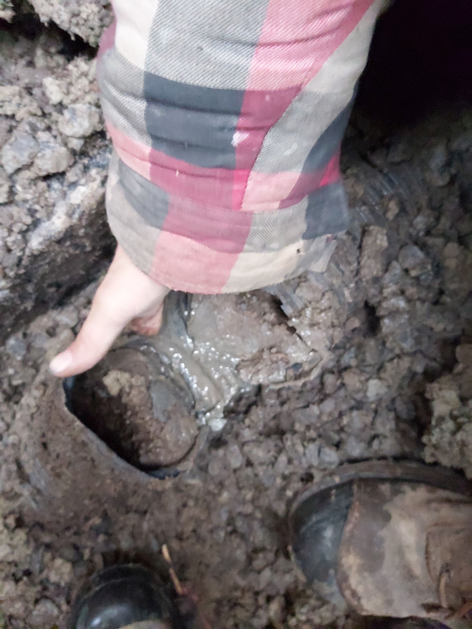Une personne portant une chemise à carreaux et des bottes noires se tient debout dans la boue.