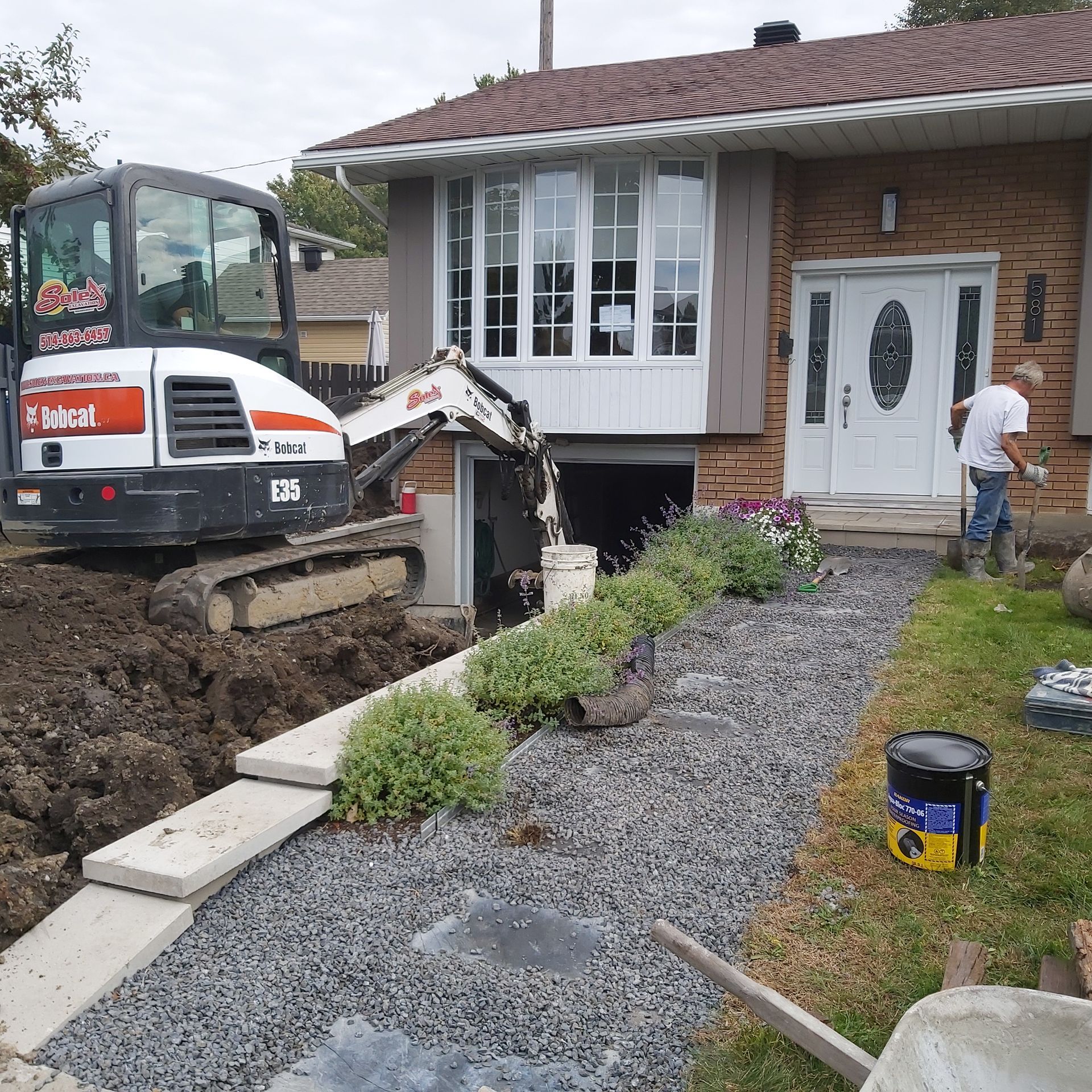 Une excavatrice Bobcat creuse un trou devant une maison