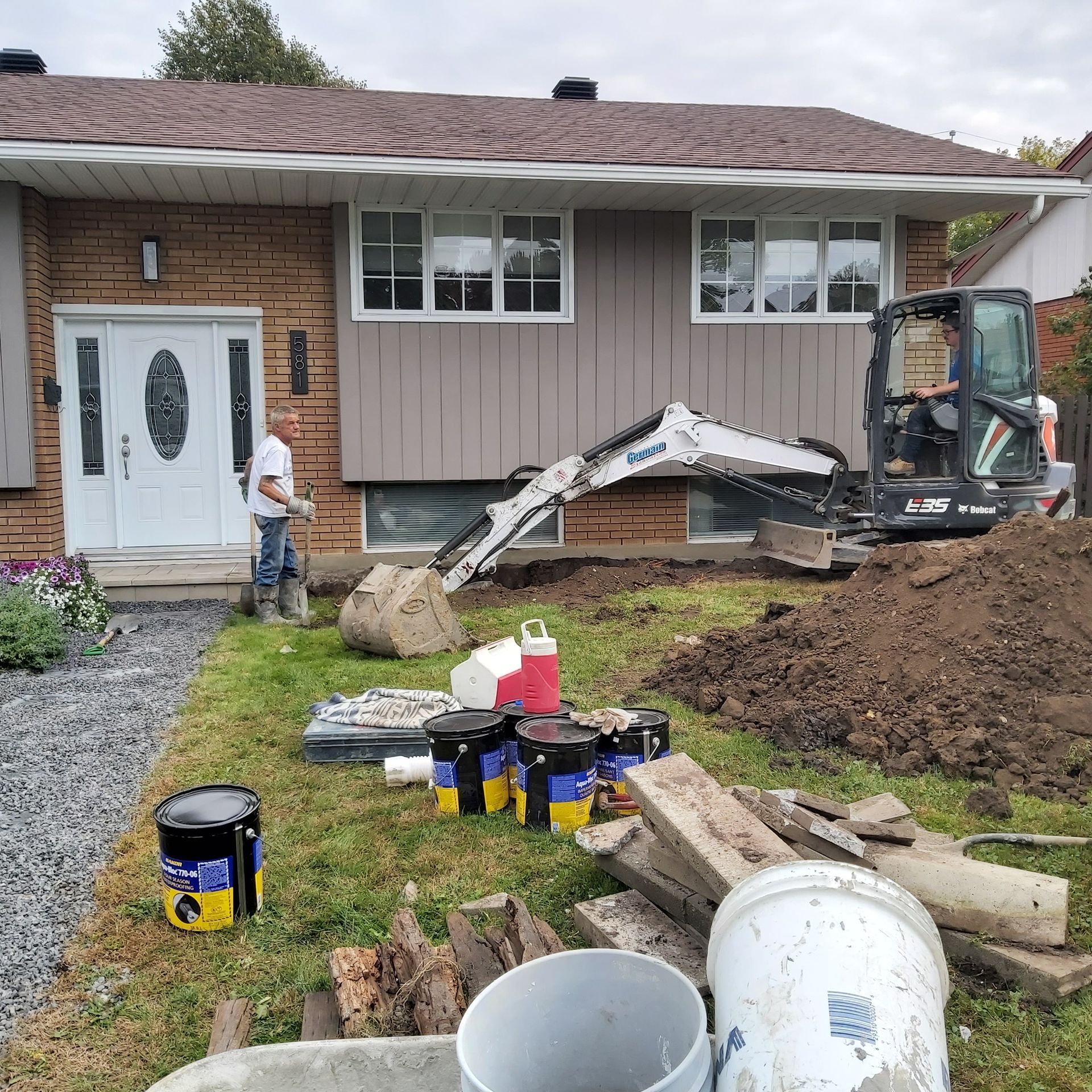 Un homme se tient devant une maison avec une excavatrice dans l'arrière-cour