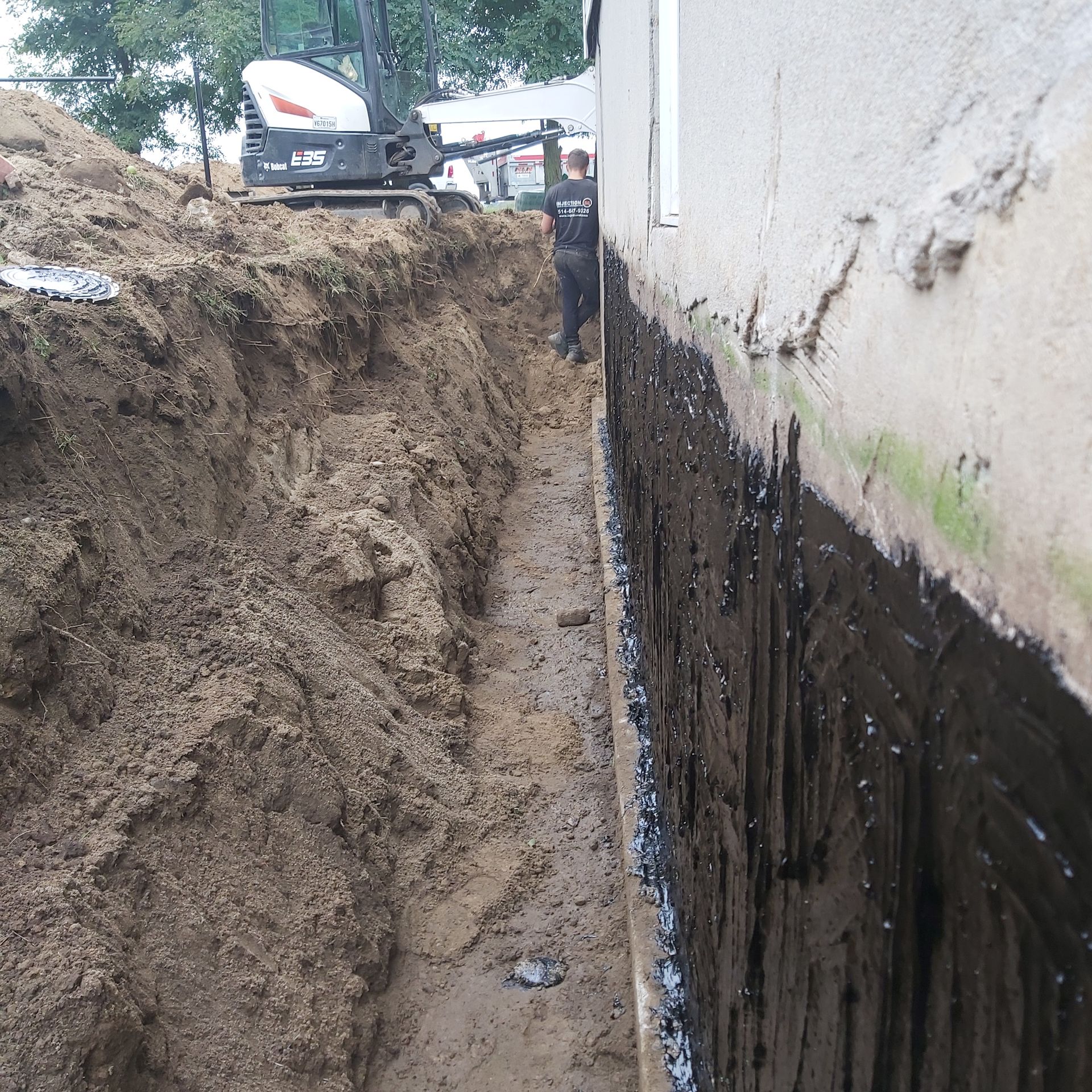 Un homme se tient dans une tranchée à côté d'une excavatrice Bobcat