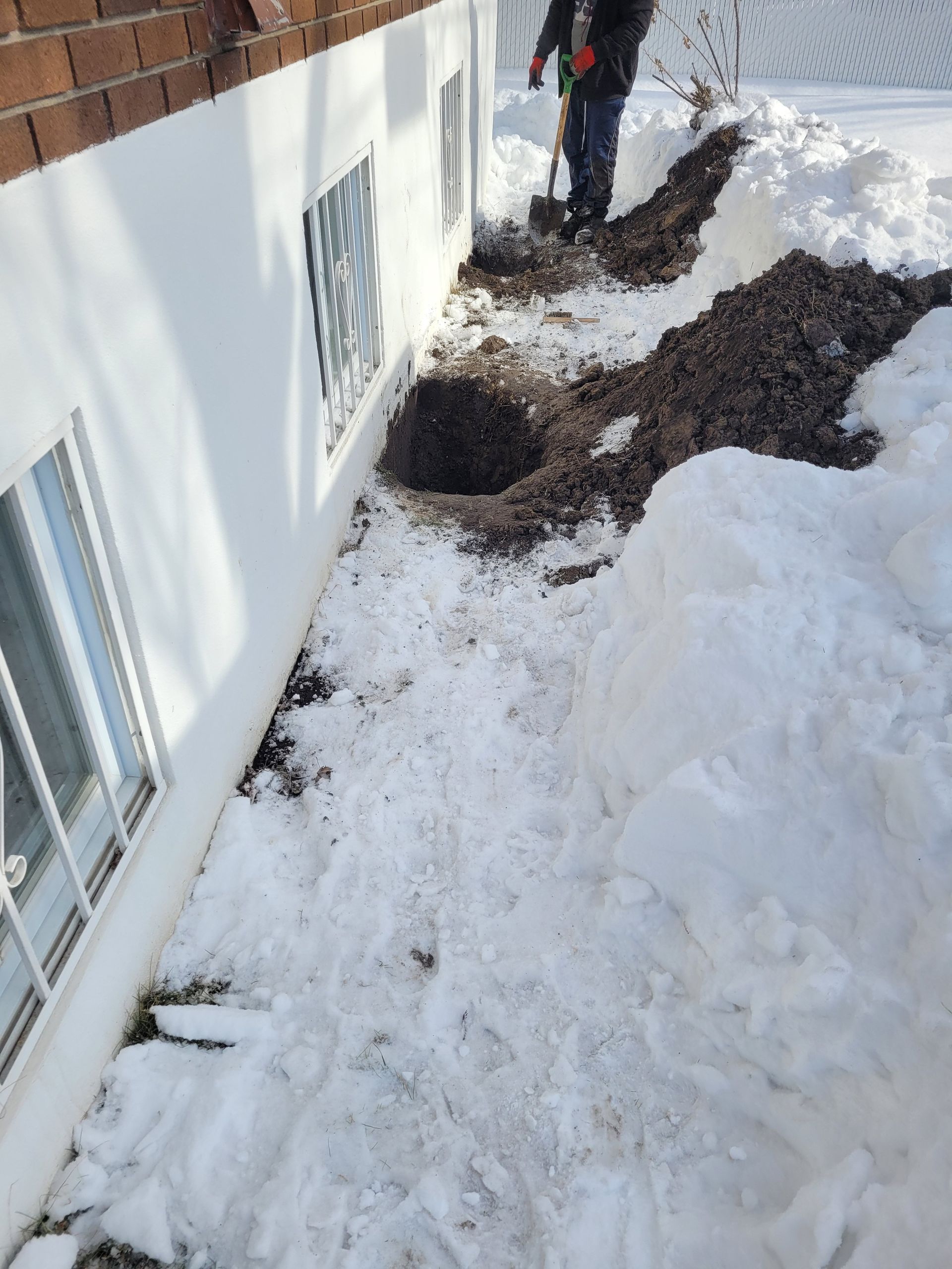 Un homme creuse un trou dans la neige devant une maison.
