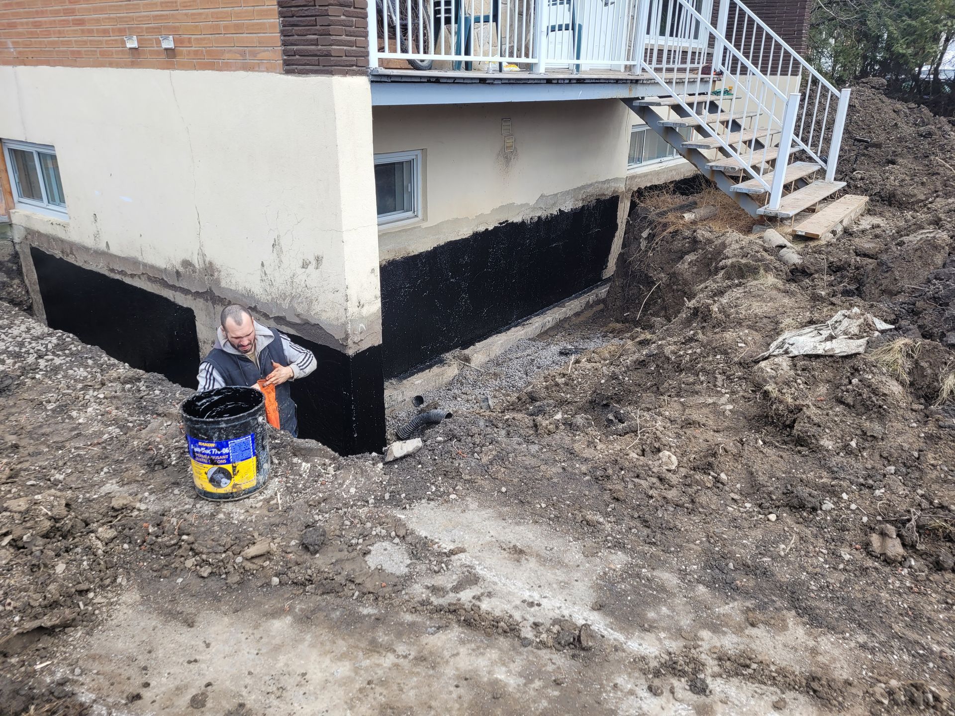 Un homme se tient à côté d'un seau de terre devant une maison.
