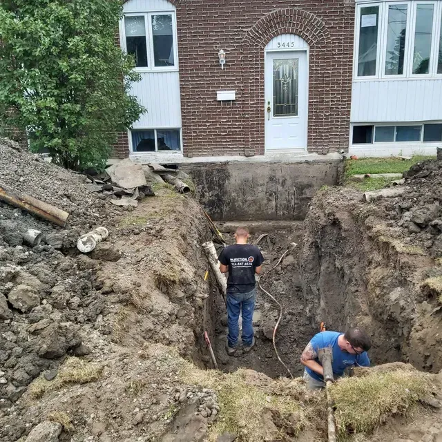 Deux hommes creusent un trou devant une maison en briques.