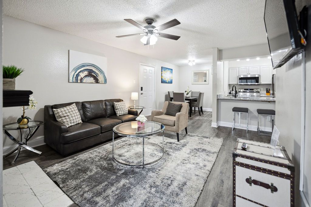 Cozy apartment living room with brown leather couch, open to kitchen and dining area, neutral color scheme.