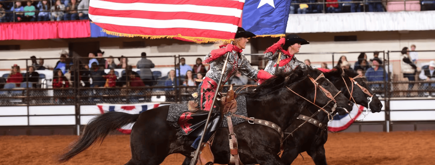 A couple of people riding horses with an american flag in the background.