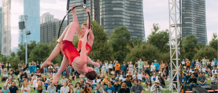 A woman is doing aerial acrobatics in front of a crowd in a park.