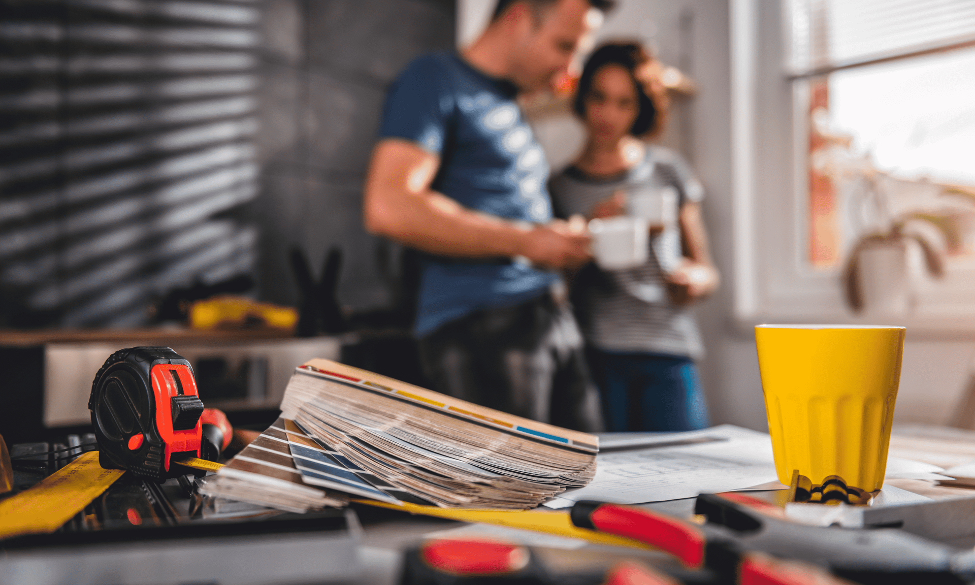 A man and a woman are standing in a kitchen looking at a blueprint.