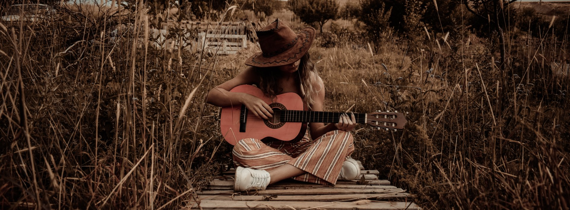 A woman is sitting on a wooden dock playing an acoustic guitar.