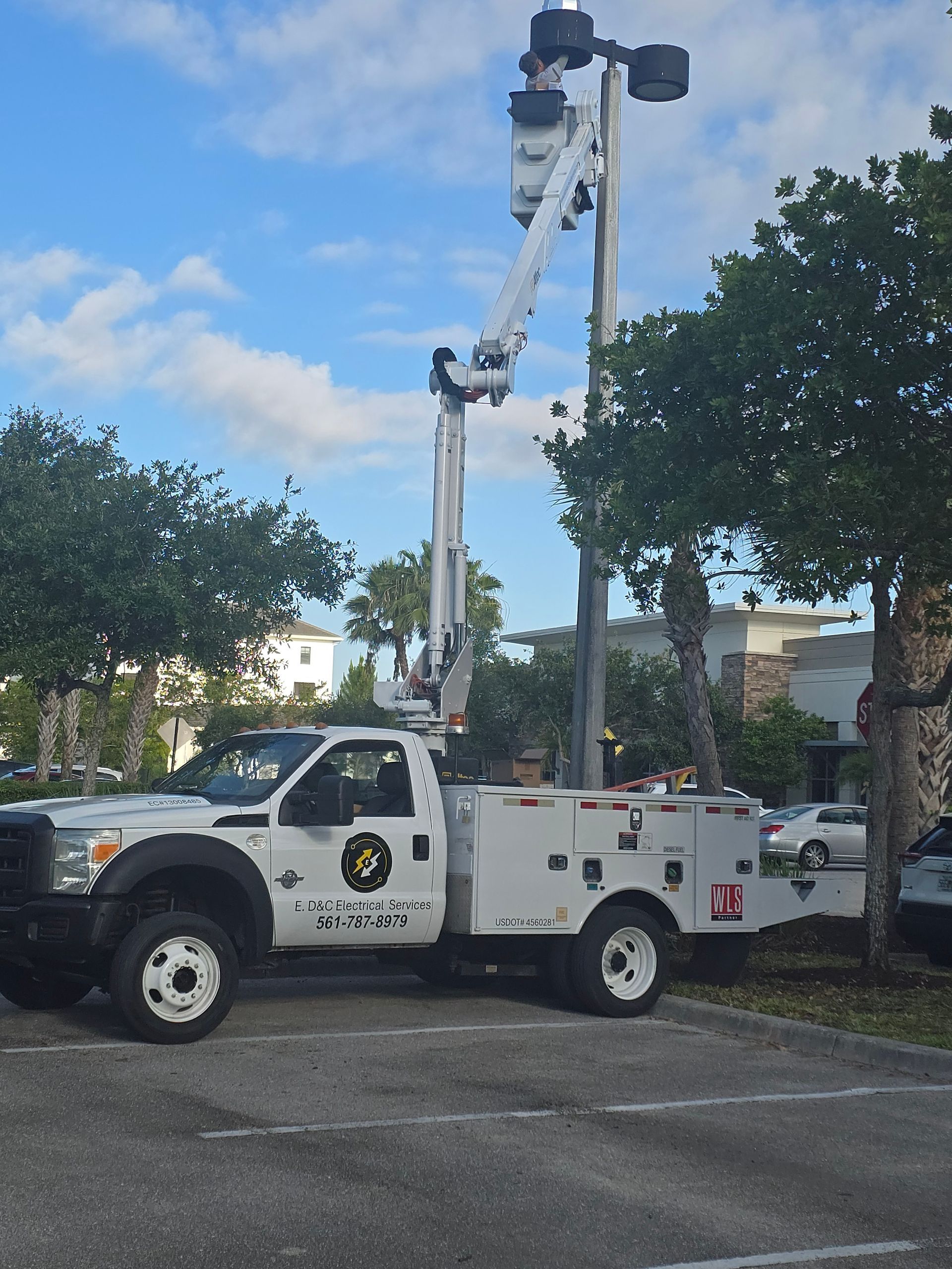Utility truck with elevated bucket lift parked beside trees in a parking lot under a blue sky