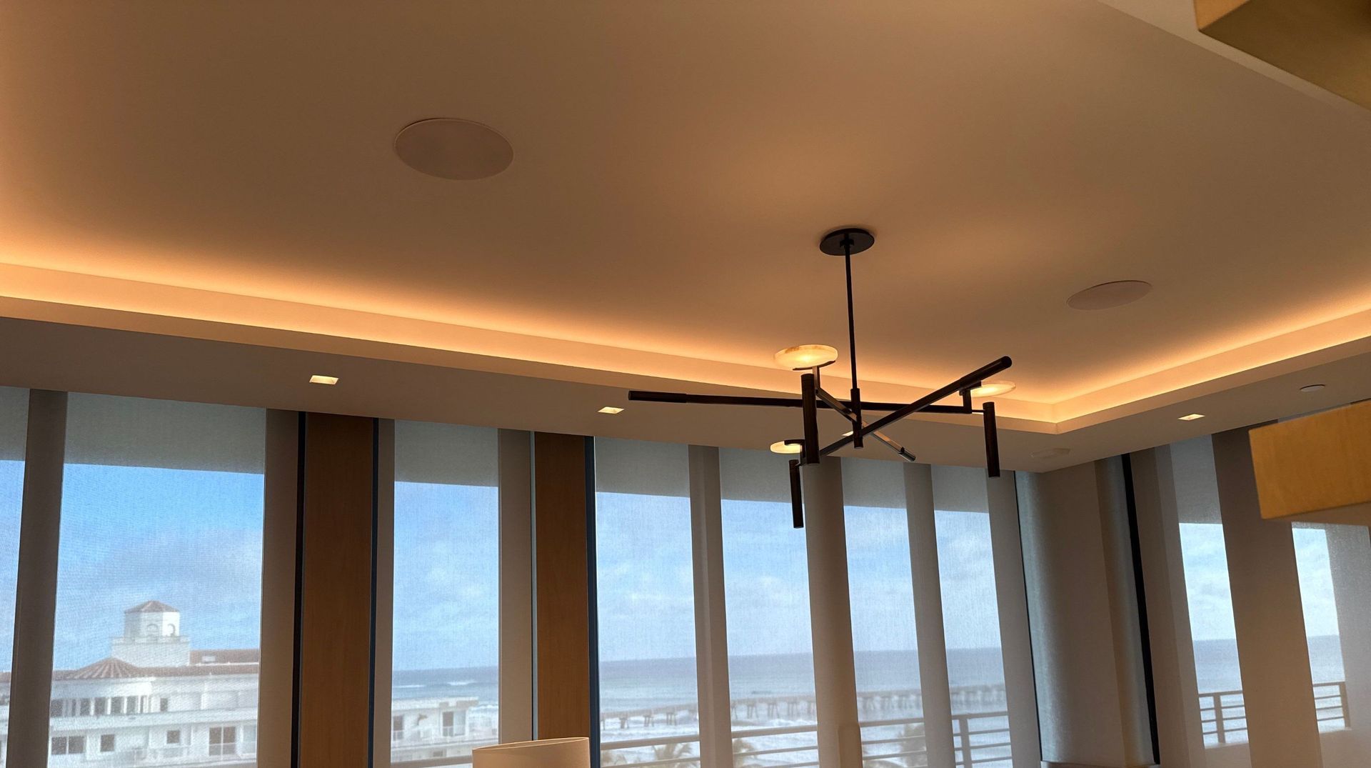 Modern room with tall windows, recessed ceiling lights, and a black chandelier overlooking a city view