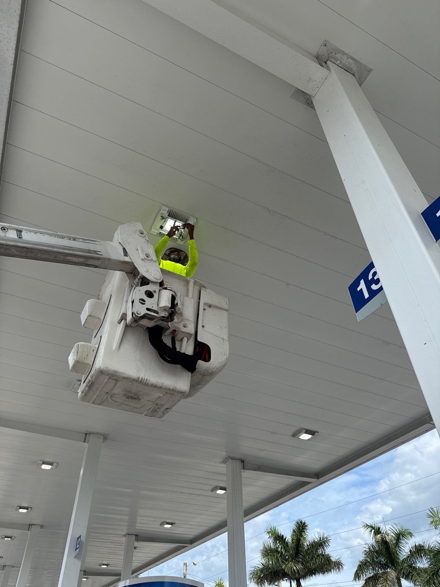 Worker in neon vest in a bucket lift inspecting a white ceiling at a covered building entrance.