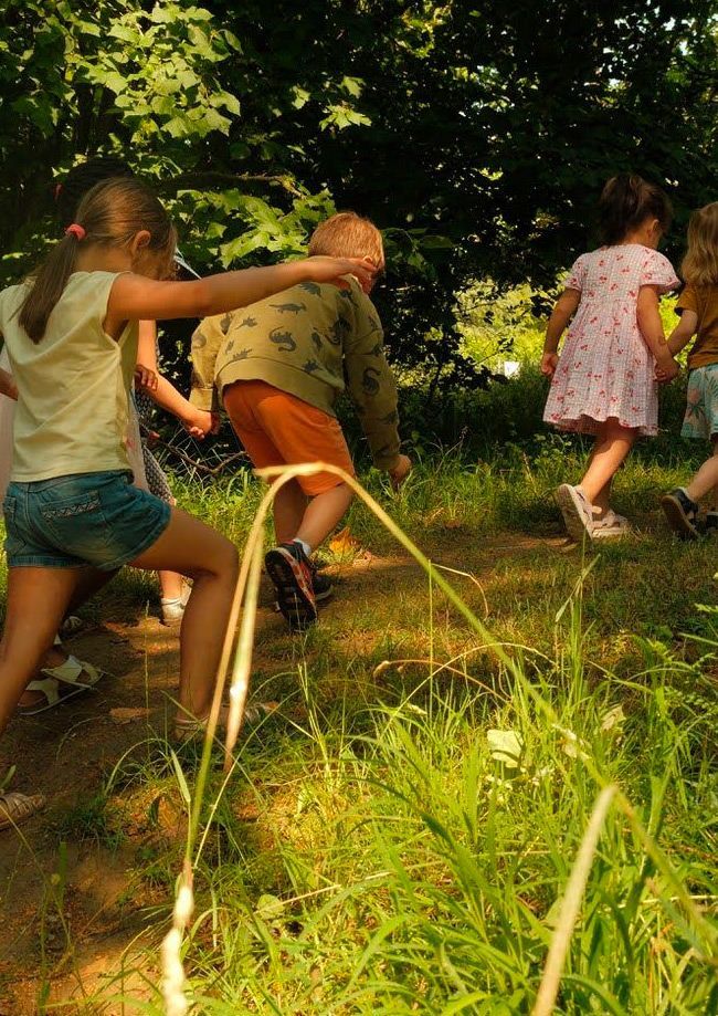 Des enfants courent dans un champ ensoleillé à l'ombre des arbres