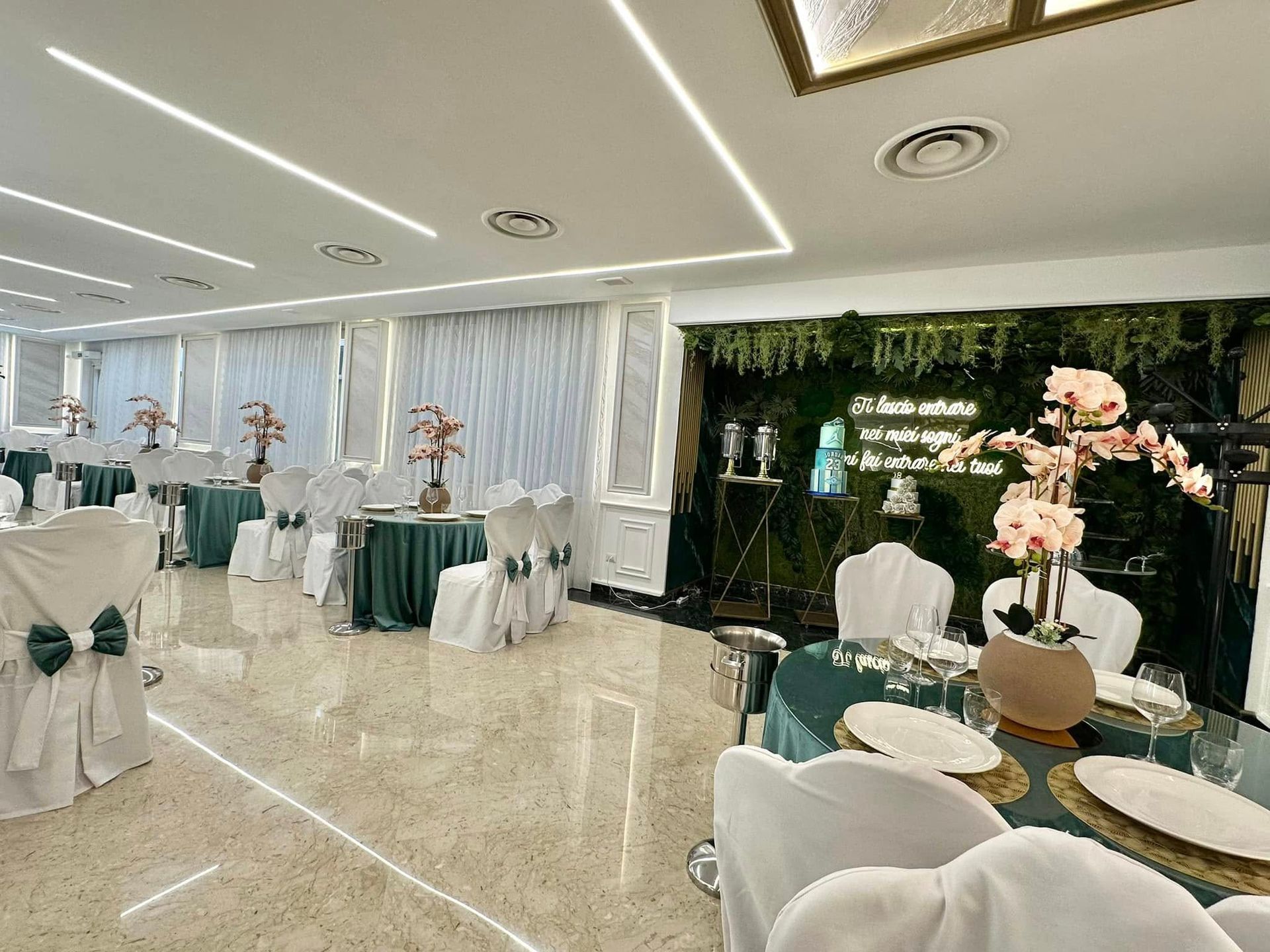 Sala da pranzo formale con tovaglie color verde acqua, coprisedie bianchi e decorazioni floreali.