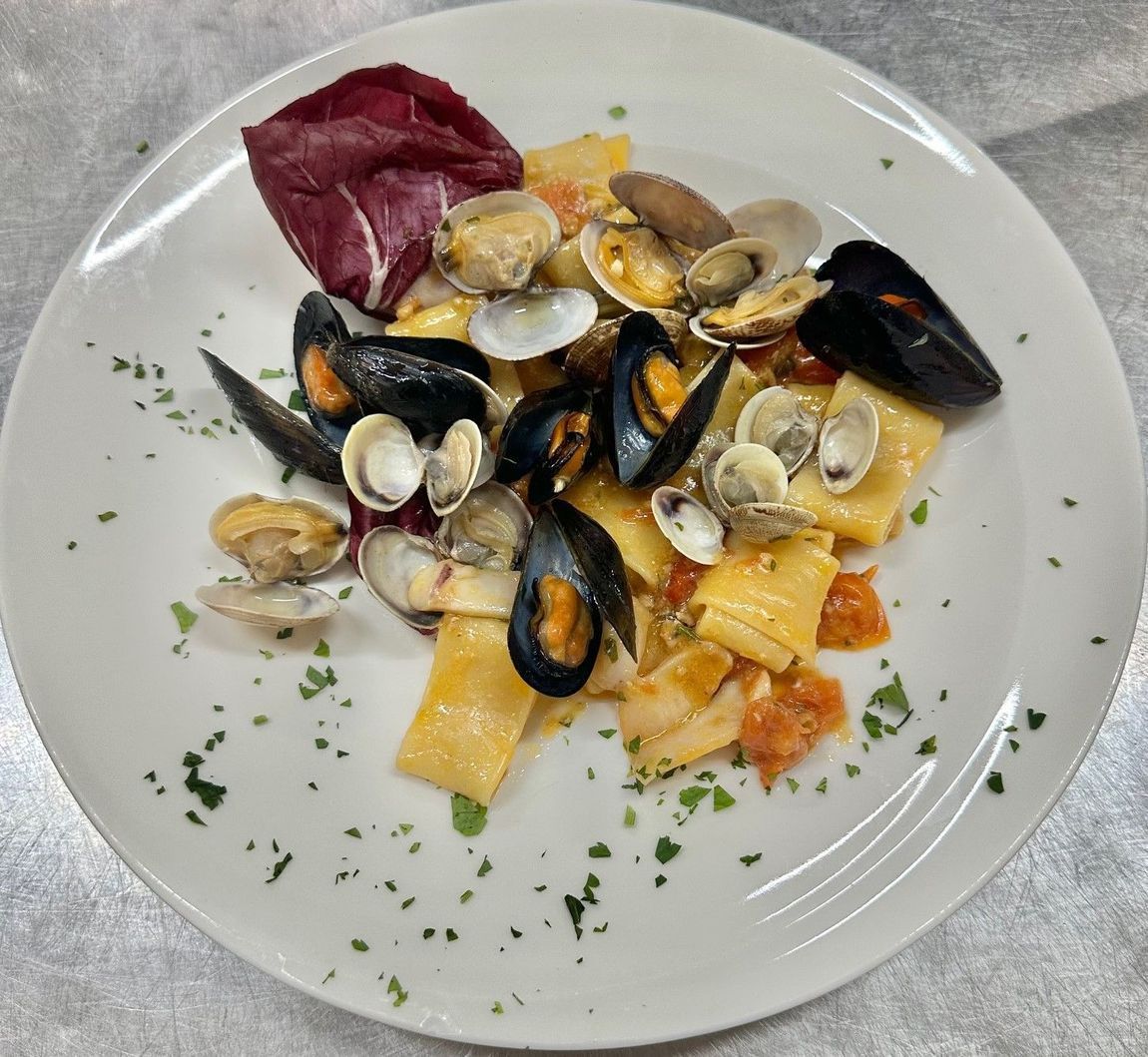 Piatto di pasta con cozze, vongole e radicchio rosso guarnito su un piatto bianco.