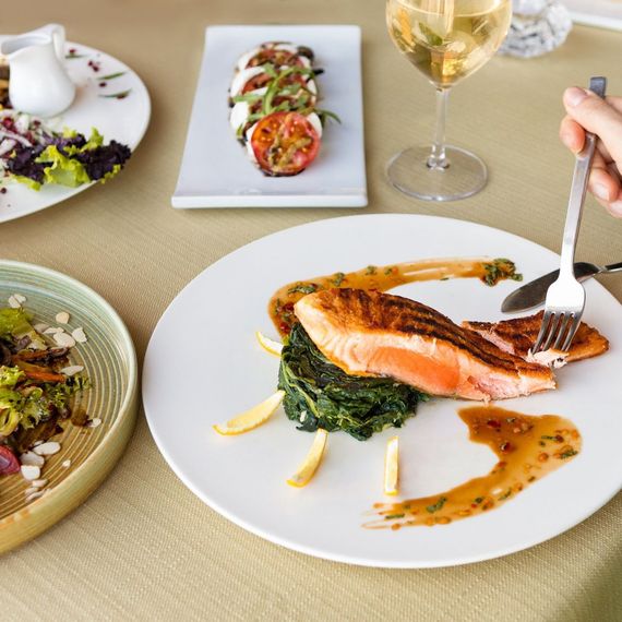 Piatto di salmone con verdure, altri piatti e un bicchiere di vino su un tavolo.