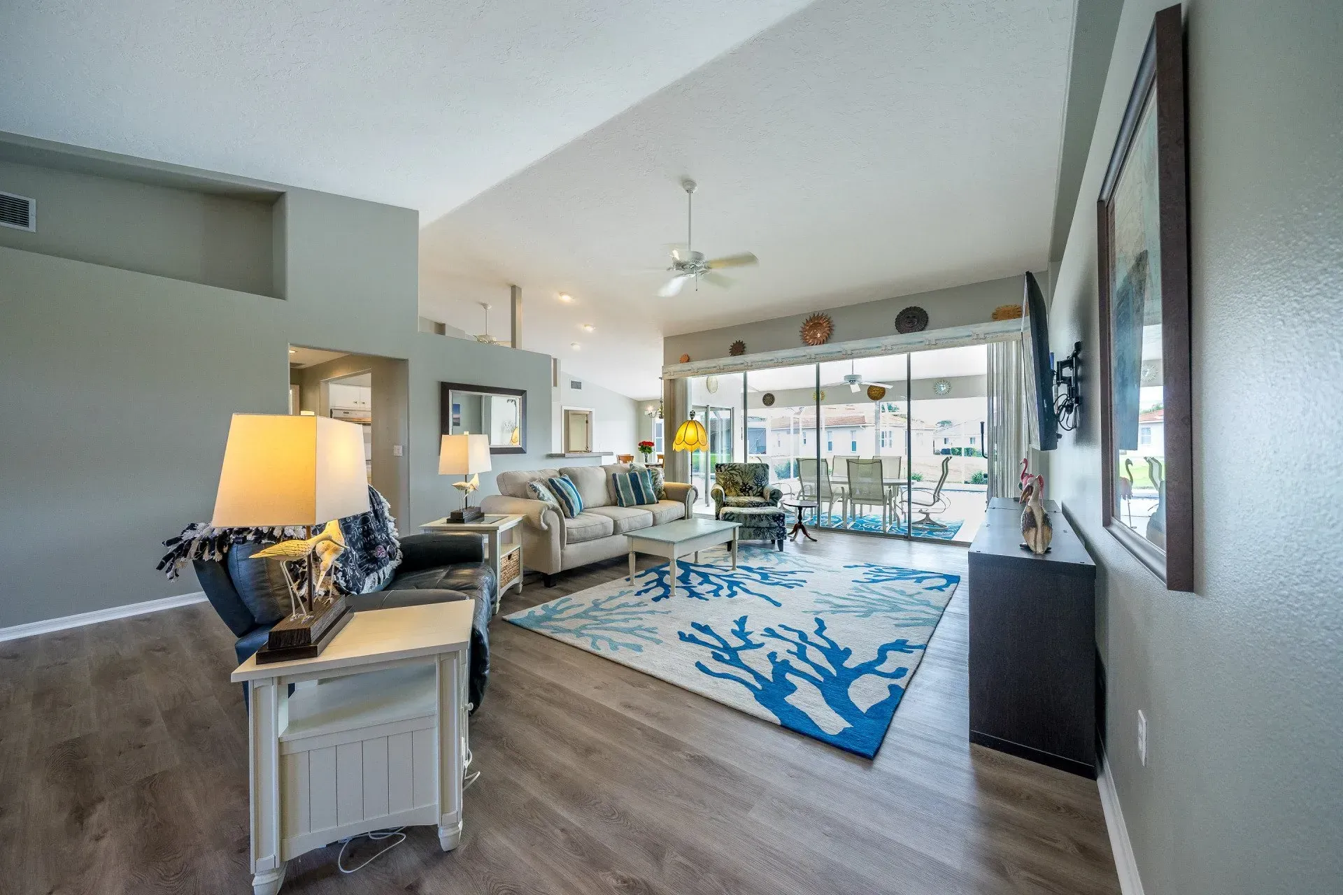 Spacious living room with gray walls, wood flooring, and blue coral rug, with sliding glass doors leading to a patio.