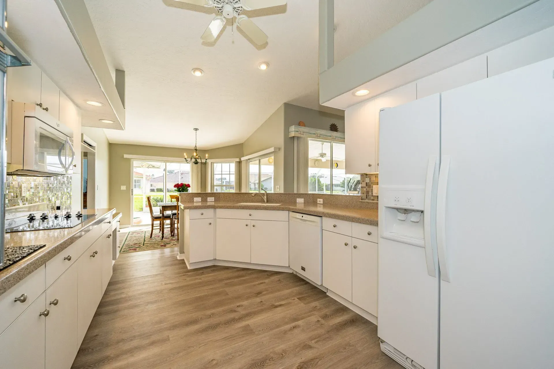 Bright white kitchen with a refrigerator, cabinets, countertops, and flooring, leading to a dining area.