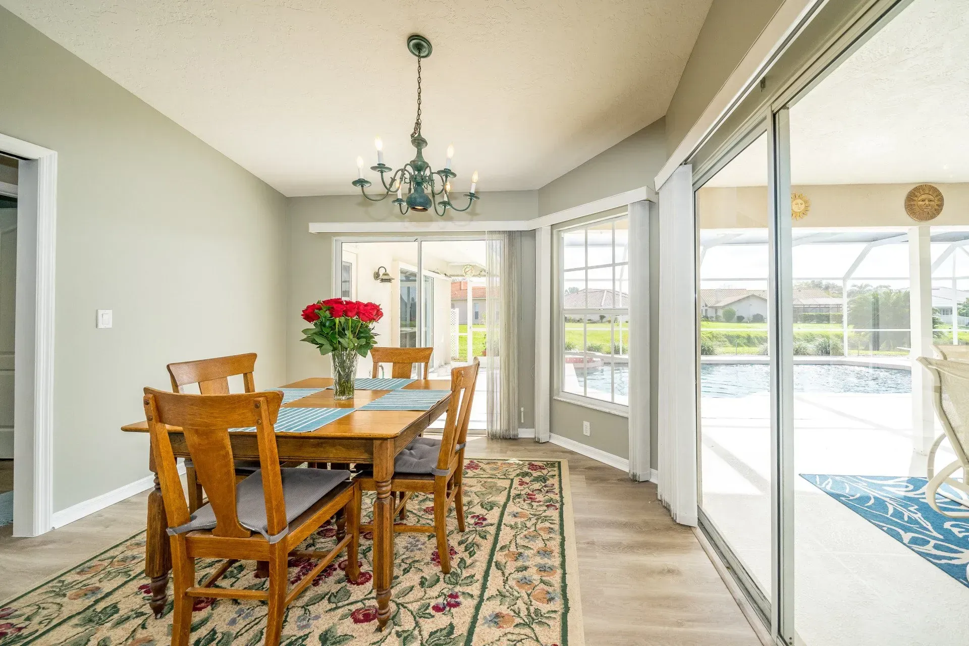 Dining room with wooden table and chairs, chandelier, and sliding glass doors to a pool.