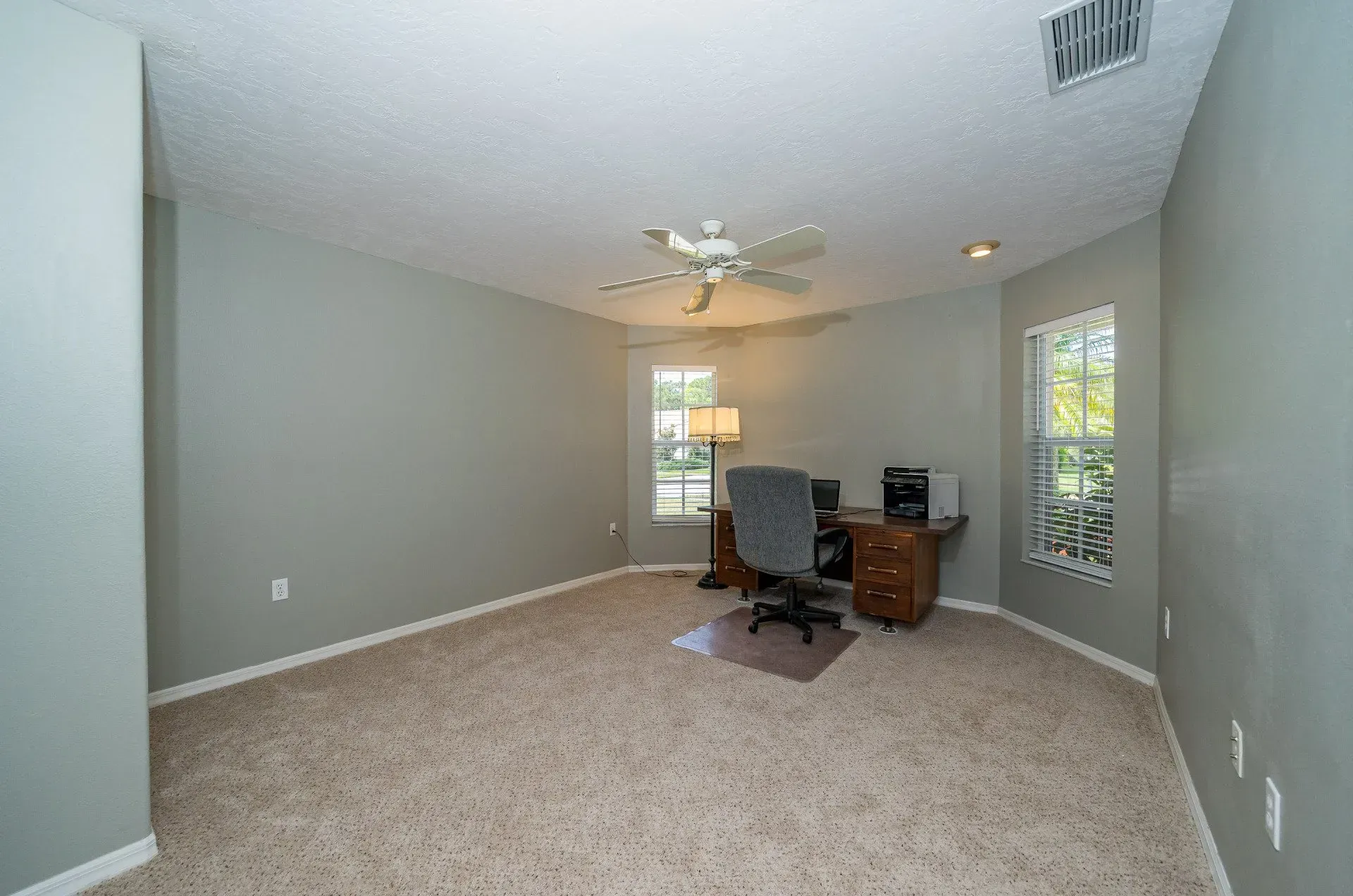 Empty home office with gray walls, beige carpet, and a wooden desk.