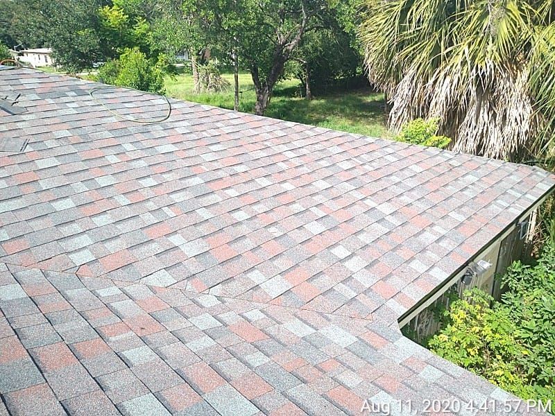 Asphalt shingle roof with mixed colors, overlooking a yard with trees.