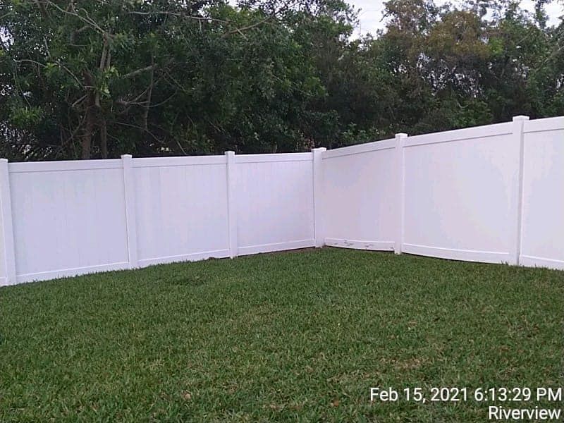White vinyl fence in a grassy yard, trees in the background.