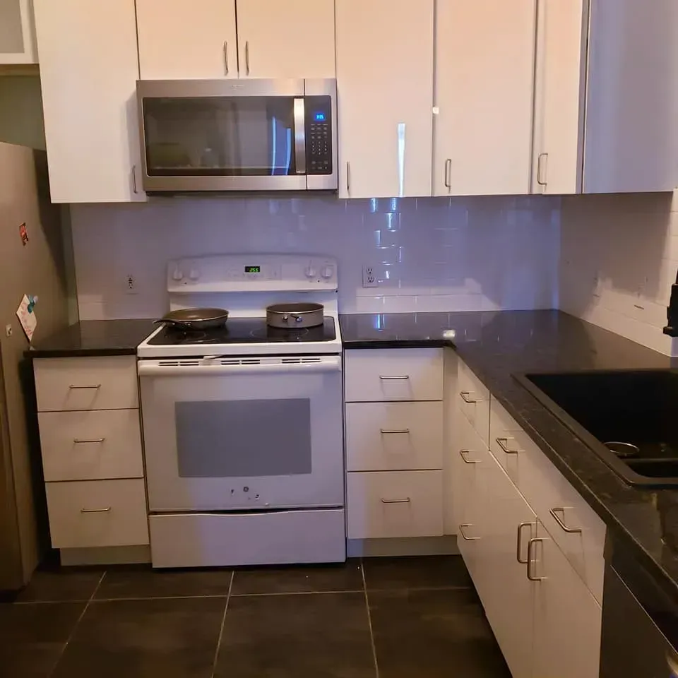 Kitchen with white cabinets, black countertops, stainless steel appliances, and dark floor tiles.