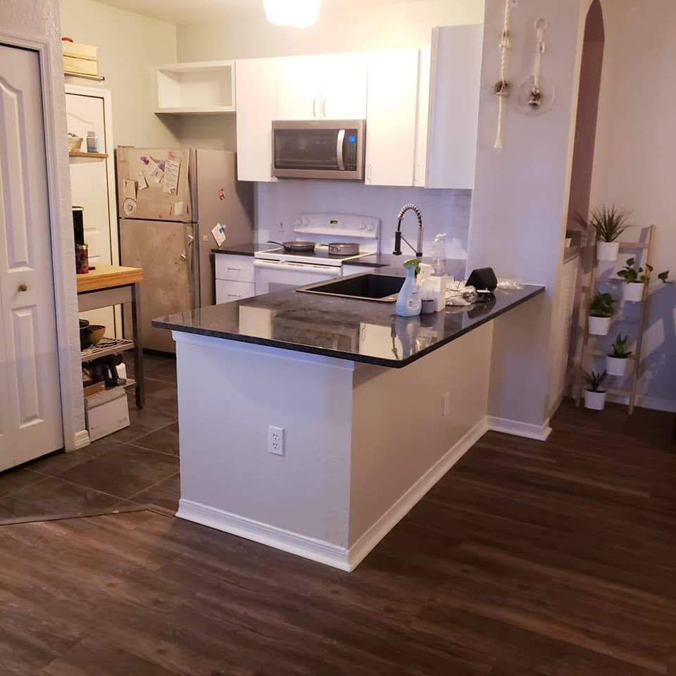 Kitchen with white cabinets, stainless steel appliances, black countertop island, and dark wood flooring.
