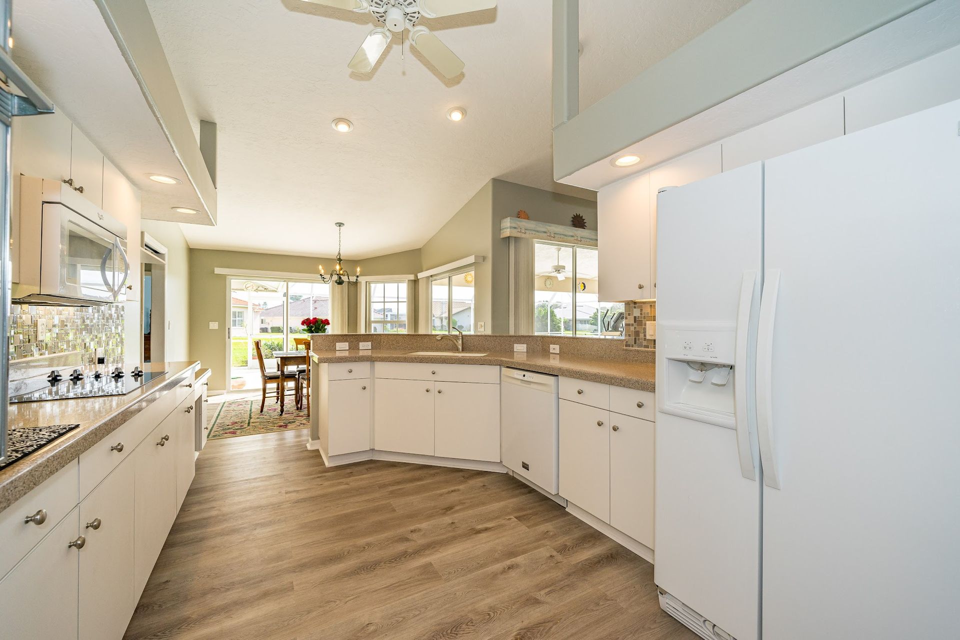 Bright white kitchen with light wood-look floor, appliances, and a dining area visible in the background.