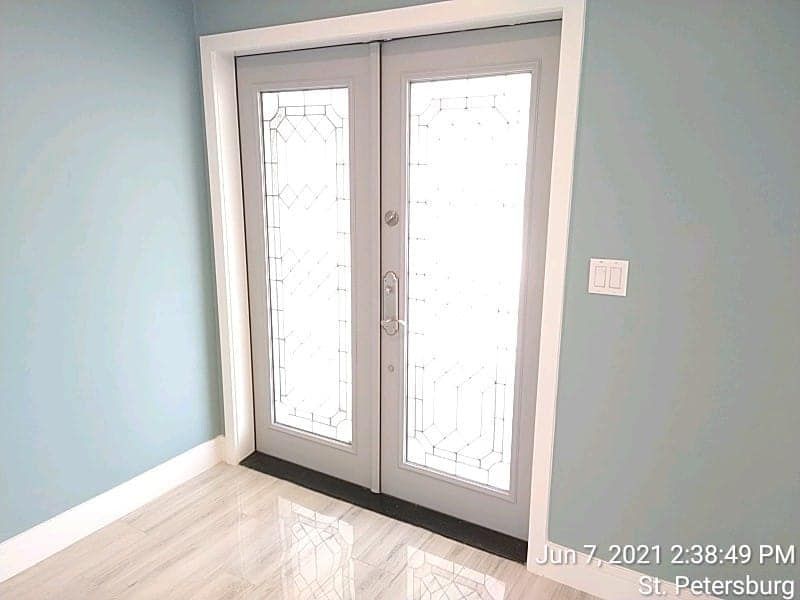 Double glass doors with intricate designs, white trim, light blue walls, and a light-colored floor.