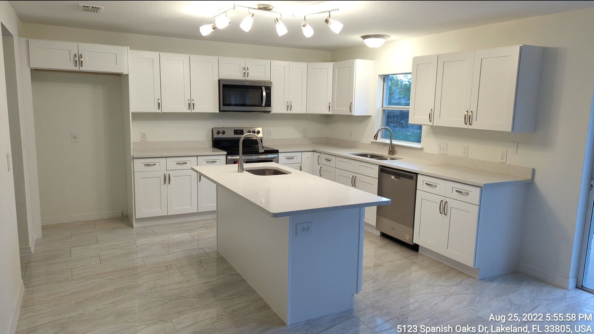 White kitchen with island, cabinets, stainless steel appliances, and tile floor.