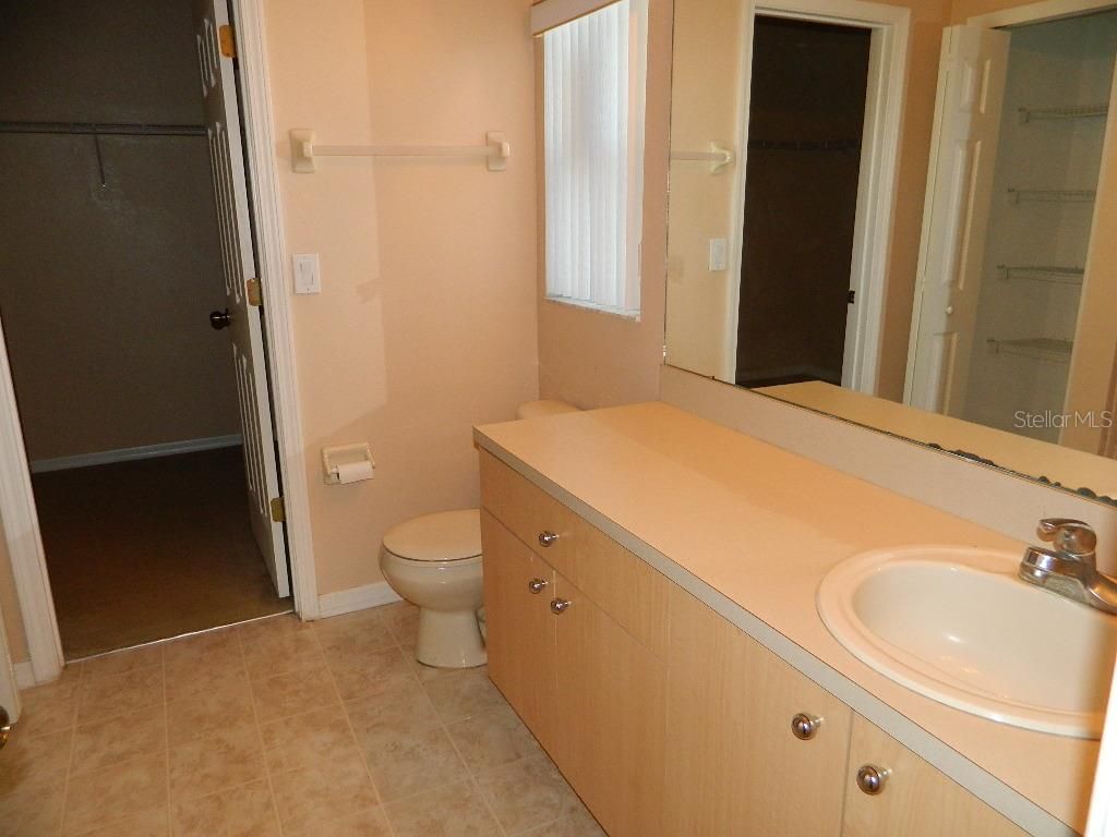 Bathroom with a beige vanity, toilet, and a walk-in closet in the background.