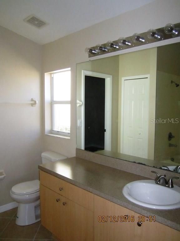 Bathroom with light brown vanity, large mirror, and toilet.