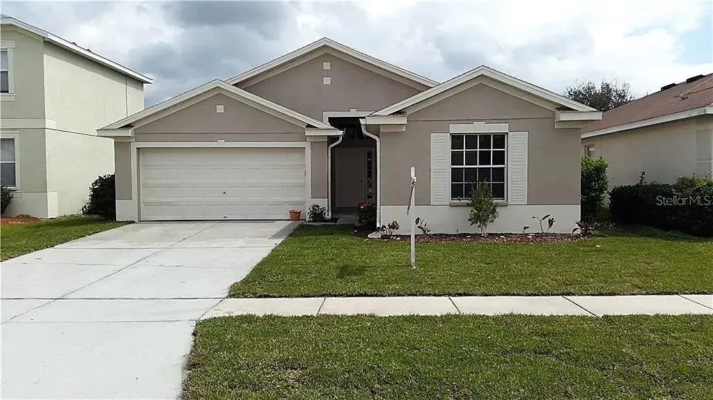 Beige suburban house with a two-car garage, front door, and a small front yard with green grass.