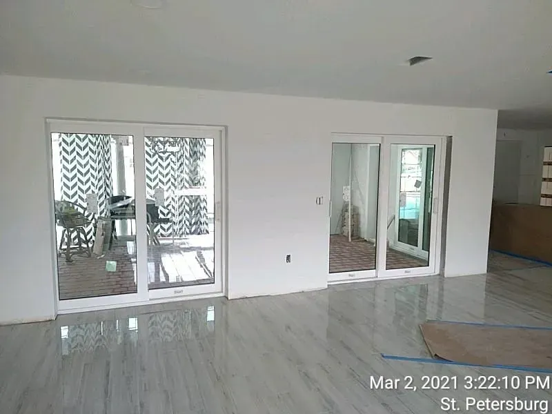 Interior view of a room with two white sliding glass doors, reflective gray floor, white walls, and bright lighting.
