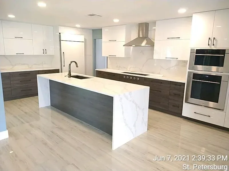 Modern kitchen with white and gray cabinets, island, stainless steel appliances, and marble countertops.