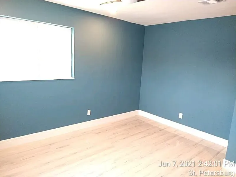 Empty room with teal walls, white trim, window, and light wood flooring.
